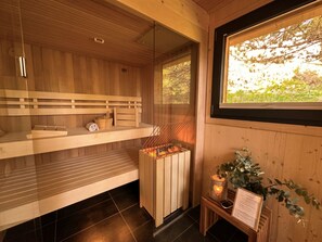 Ein Saunaraum mit Holzbänken, einer Saunaanlage und einem Fenster mit Blick auf Bäume.
