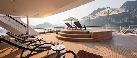 A sun deck with lounge chairs, umbrellas, and a central seating area on a cruise ship.