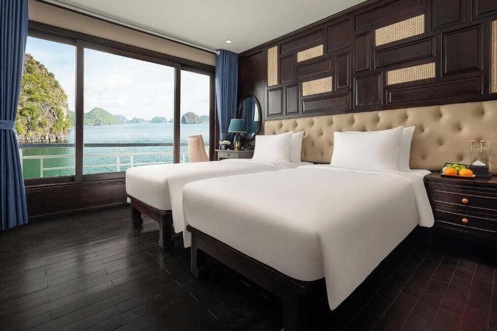 Een hotelkamer met twee bedden, een groot raam met uitzicht op een wateroppervlak en groen, en een donker houten paneel hoofdeinde.