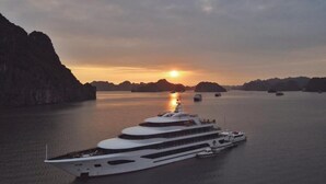 En stor, vit lyxyacht låg förtöjd i stilla vatten, med en solnedgång i bakgrunden.