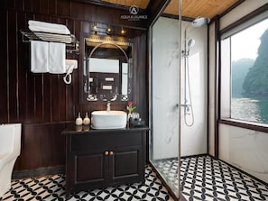 A bathroom with a dark wood vanity, a white sink, a mirror, and a shower. - Lan ha bay luxury cruise (Tuan Chau)