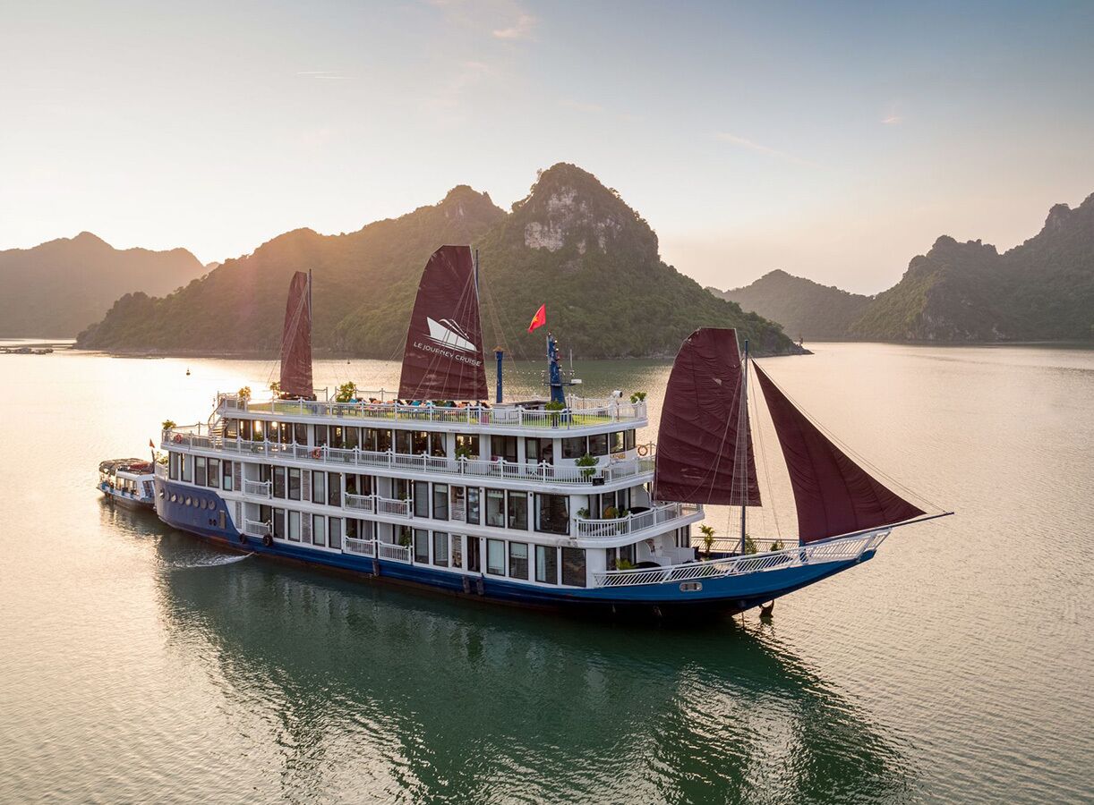 A multi-deck river cruise boat with a flag, set against a mountainous backdrop.