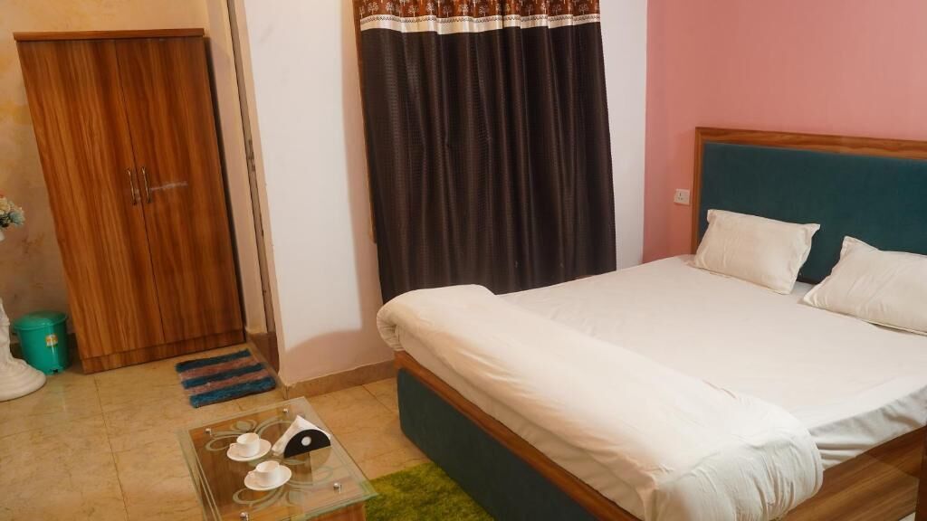 A bedroom with a bed, a wardrobe, a window with curtains, and a small table with cups and saucers.