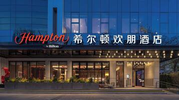 A modern hotel entrance with a glass facade, a prominent sign, and a well-lit outdoor seating area.