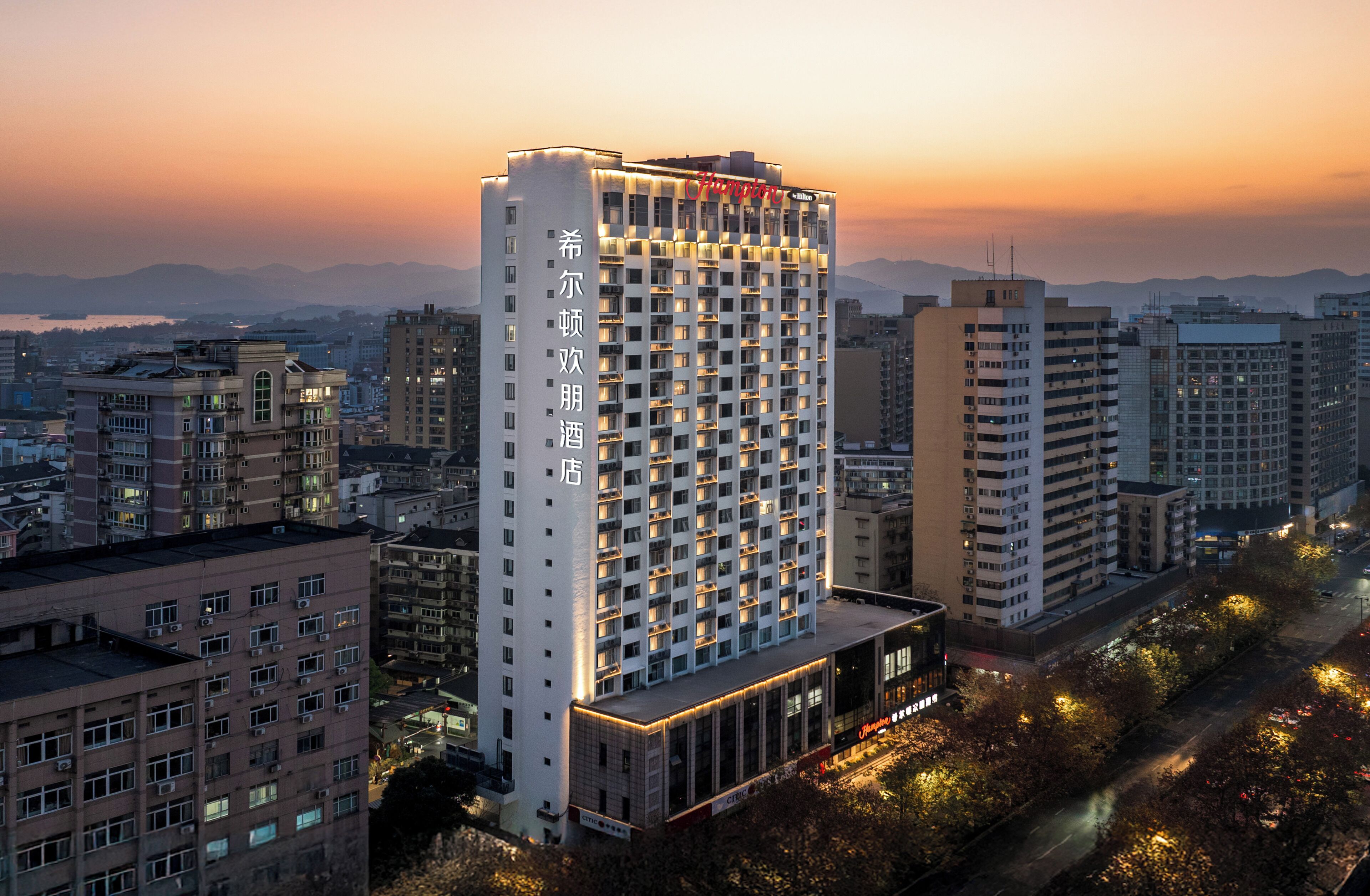 Un hotel de gran altura con varios pisos, un letrero llamativo y vistas del paisaje urbano al atardecer.