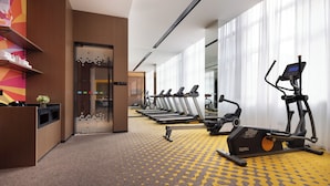 Ginásio de hotel com equipamentos de exercício, uma receção e uma parede colorida.