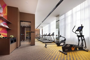 A hotel gym with exercise equipment, a reception desk, and a colorful wall.