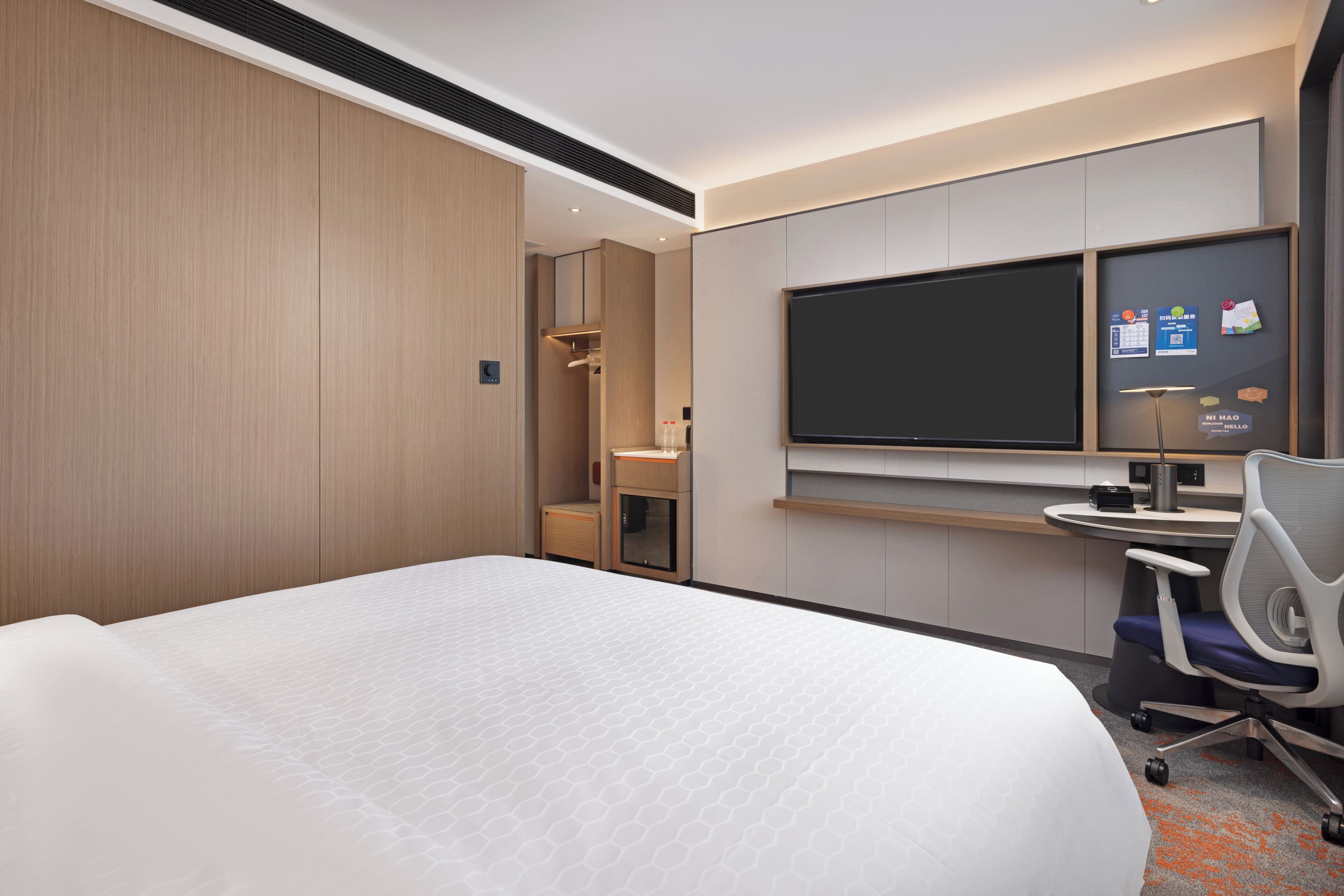 A hotel room with a large bed, a desk with a chair, a flat-screen TV, and a wardrobe.