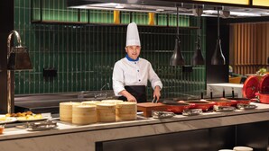 Um chef em uma cozinha profissional com eletrodomésticos de aço inoxidável, painel de azulejos verdes e diversos utensílios e panelas de cozinha.