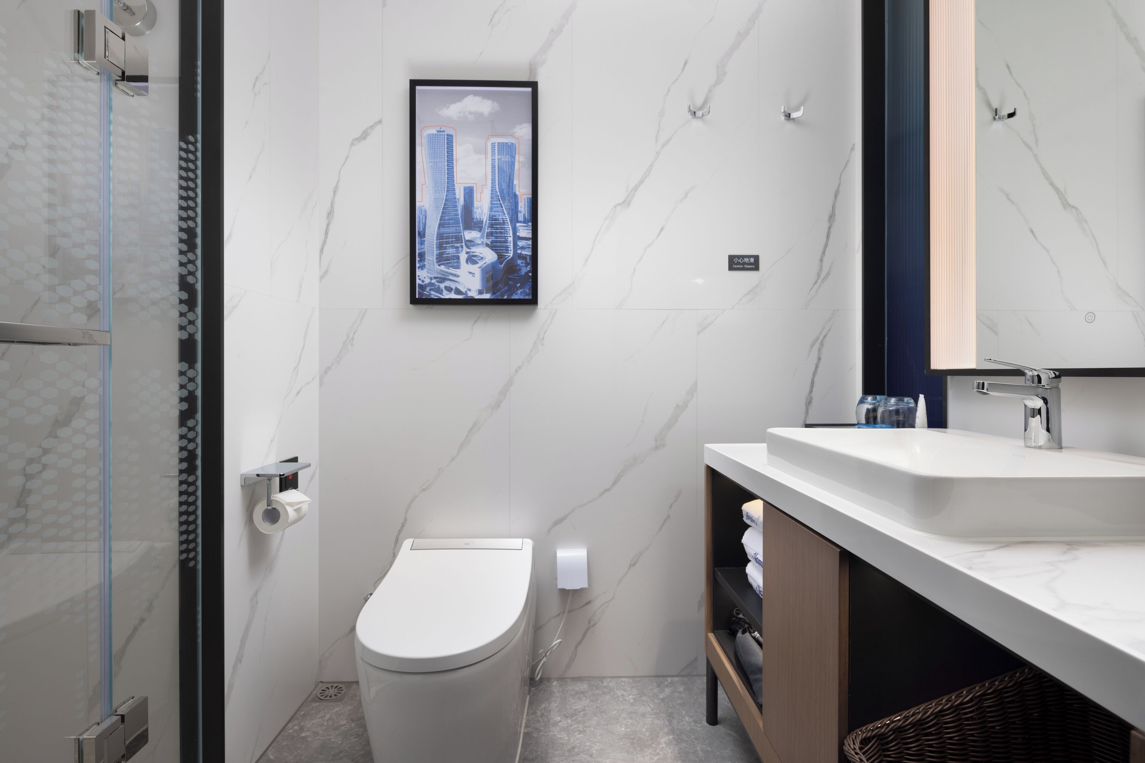 A modern bathroom with a toilet, a framed cityscape picture, a shower area, and a vanity with a mirror.