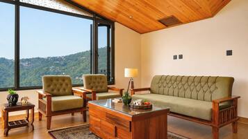 Una habitación con un ventanal grande, un sofá, dos sillones, una mesa de centro de madera y una mesita auxiliar con una lámpara.