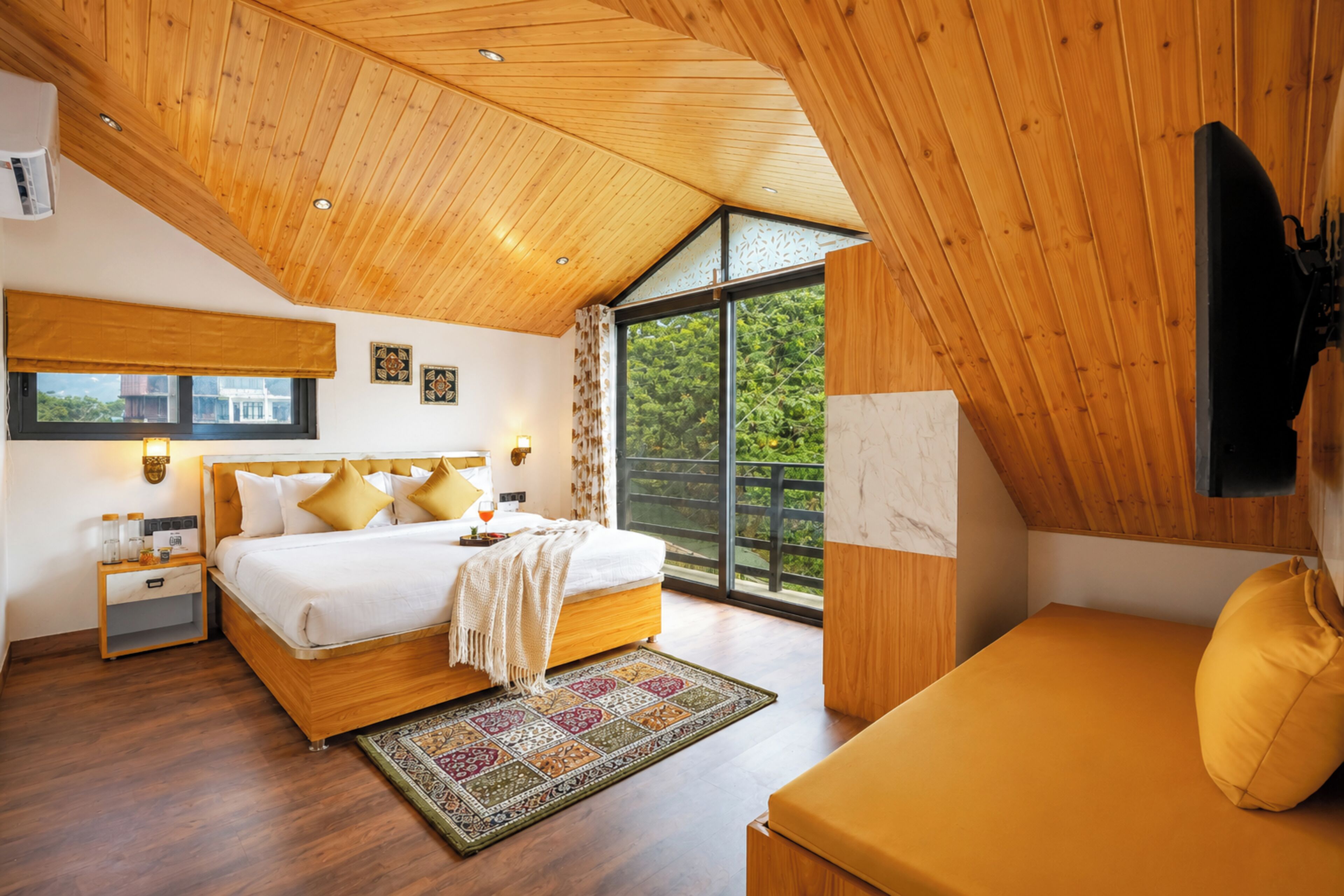 A bedroom with a large bed, bedside tables, a sofa, a window, and a ceiling with wooden panels.