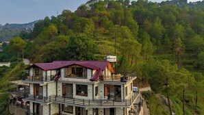 Un edificio de varios pisos con balcones, un techo rojo y vistas a una ladera boscosa.