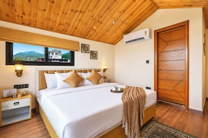 Habitación de hotel con cama, mesitas de noche, aire acondicionado, puerta de madera y vista a un edificio a través de una ventana.