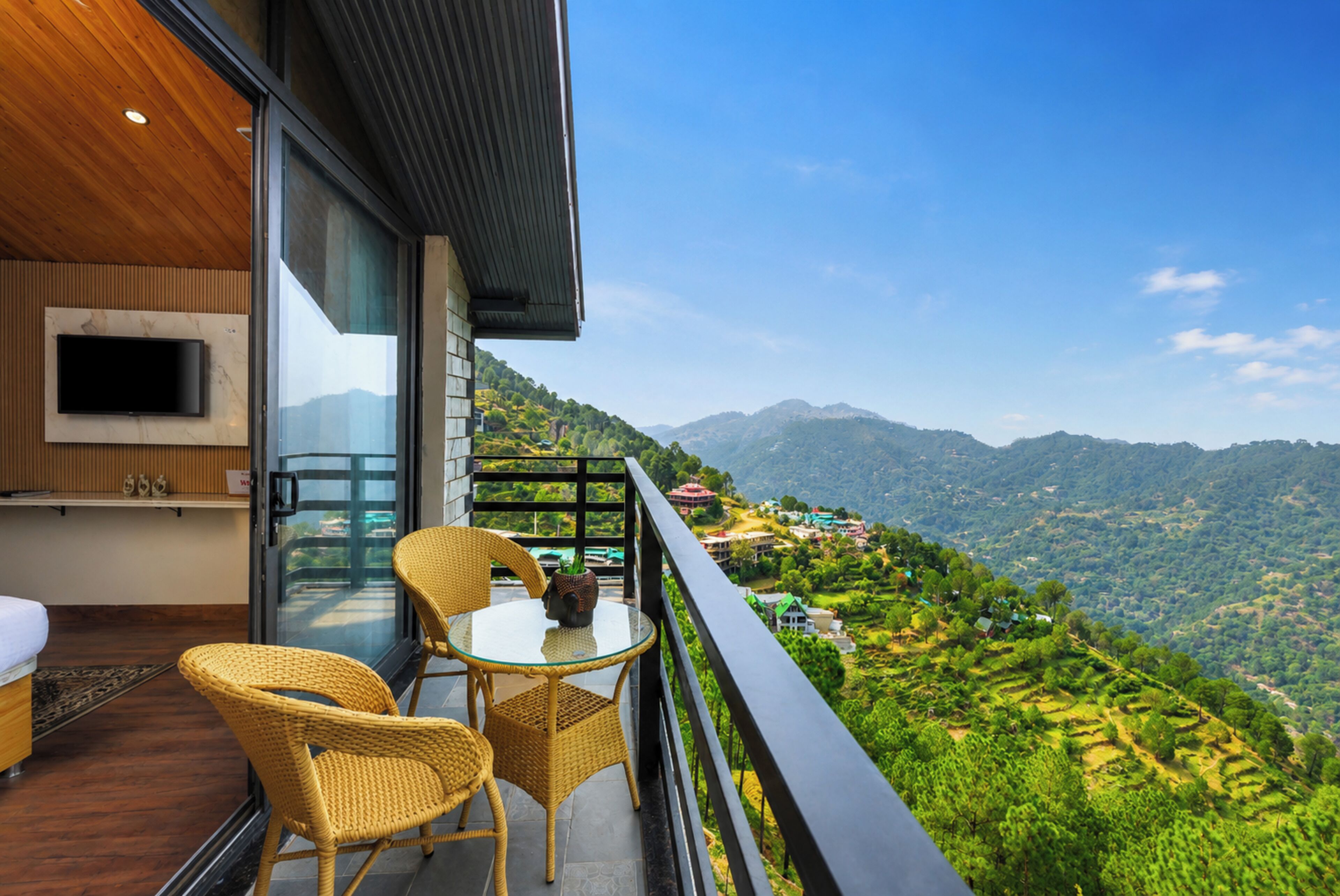 Un balcón con sillones y una mesa de mimbre, con vistas a un paisaje montañoso.