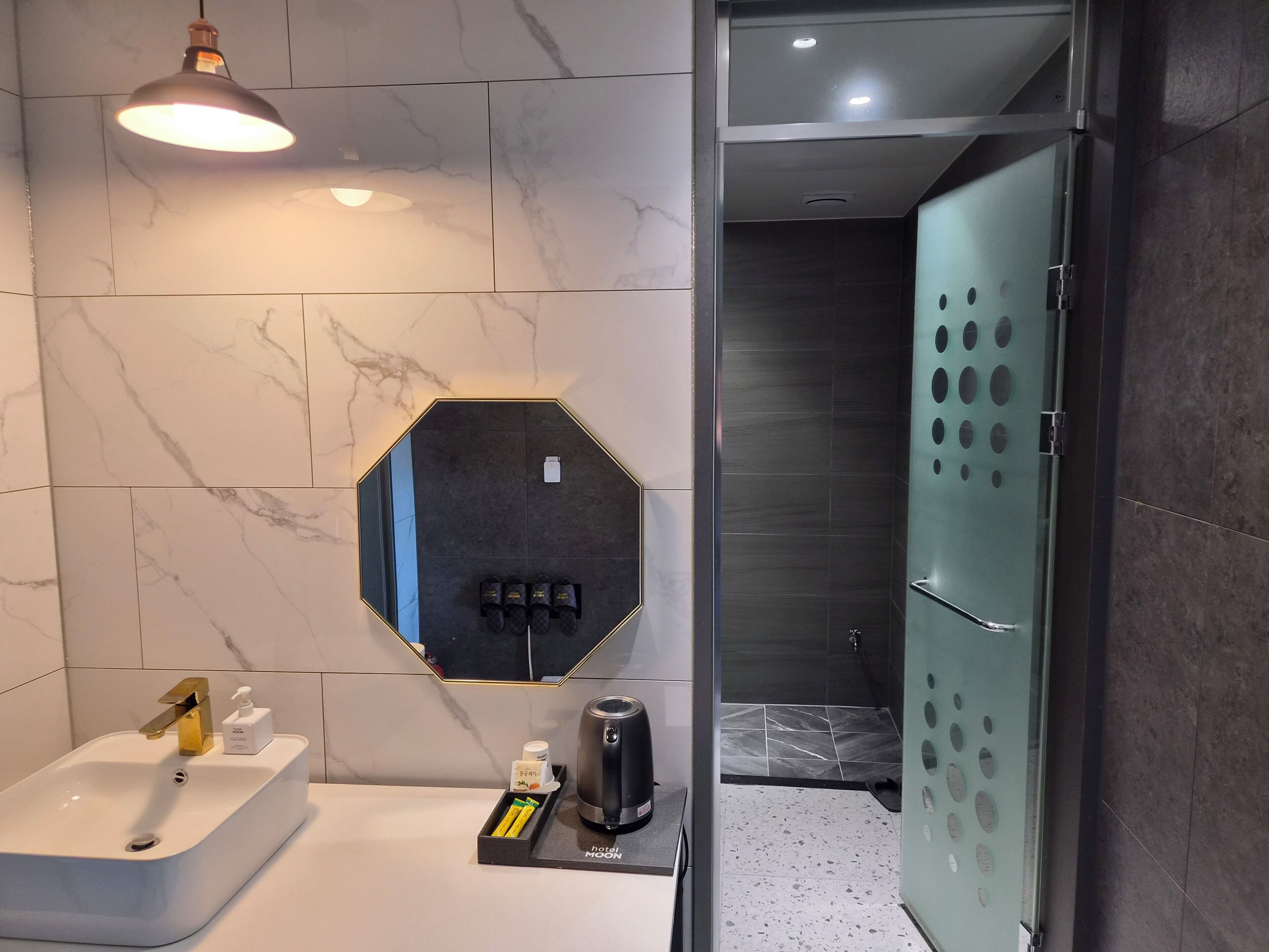 A modern bathroom with a white sink, a mirror, a towel rack, a coffee maker, and a shower area with a glass door.