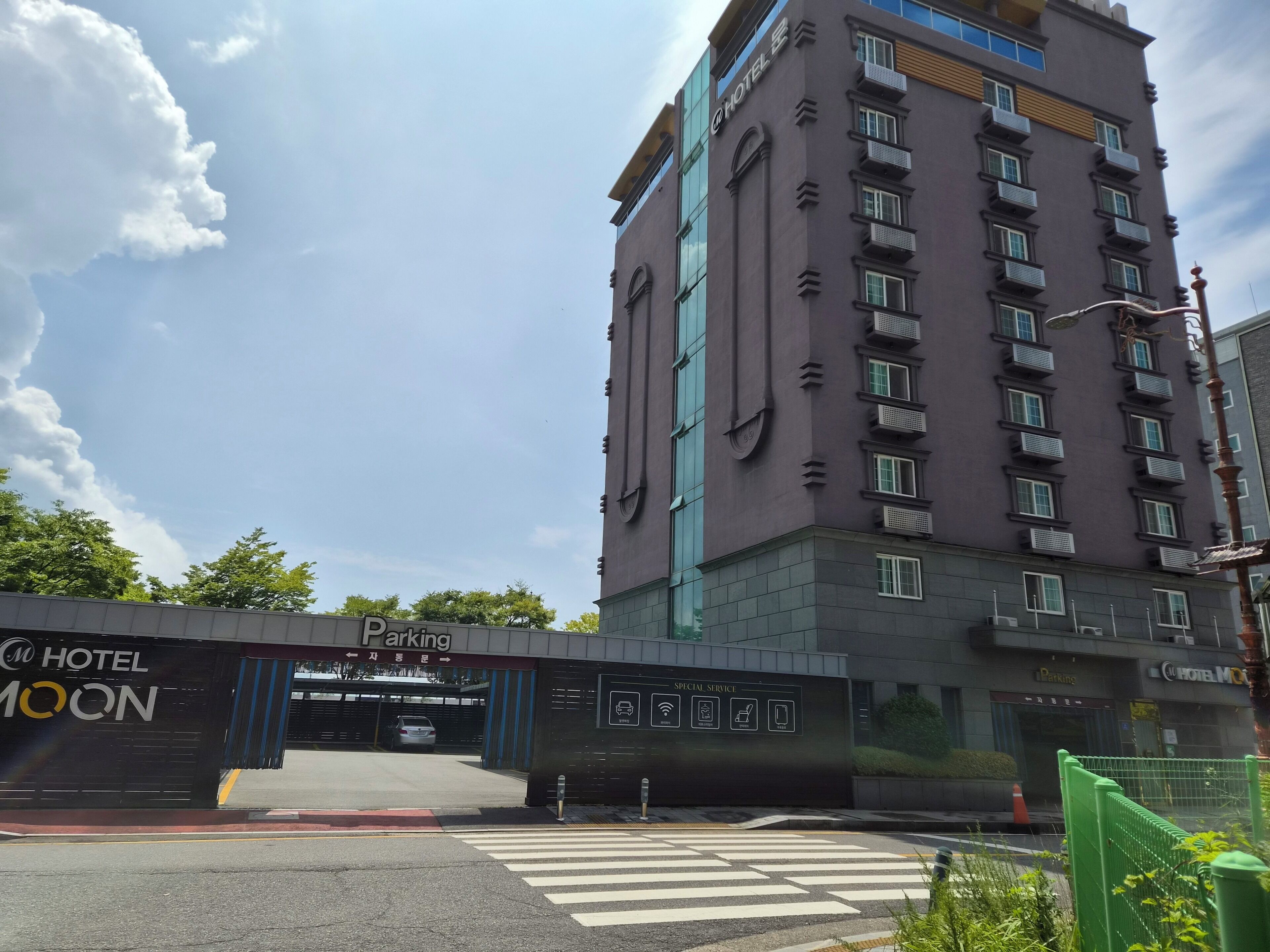 A hotel entrance with a modern design, a parking area, and a clear sky.