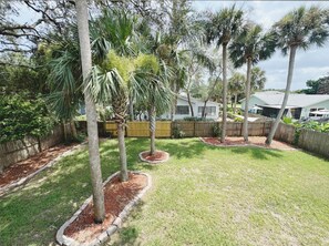 A residential backyard with a lawn, palm trees, a wooden fence, and a house in the background. - The Madonna House | Entire Beach Retreat | 6BD 4BA (St. Augustine)