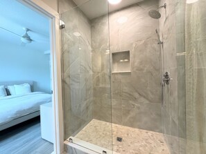 Ein modernes Badezimmer mit einer gläsernen Duschkabine, Marmorfliesen und einem Bett mit weißer Bettwäsche.