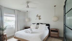 A modern bedroom with a bed, bedside tables, a ceiling fan, and a window with curtains. - The Madonna House | Entire Beach Retreat | 6BD 4BA (St. Augustine)
