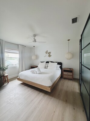 A modern bedroom with a bed, bedside tables, a ceiling fan, and a window with curtains. - The Madonna House | Entire Beach Retreat | 6BD 4BA (St. Augustine)