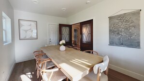 A dining room with a wooden table, six chairs, a vase with flowers, and a painting on the wall. - The Madonna House | Entire Beach Retreat | 6BD 4BA (St. Augustine)