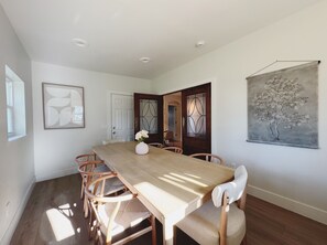 A dining room with a wooden table, six chairs, a vase with flowers, and a painting on the wall. - The Madonna House | Entire Beach Retreat | 6BD 4BA (St. Augustine)