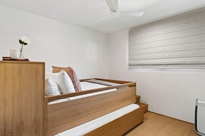A bedroom with a wooden bed, a bedside table, a nightstand, a ceiling fan, and a window with blinds.