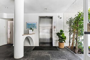 A reception area with a reception desk, a framed artwork, an elevator, and a potted plant.
