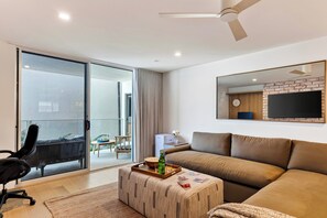 Una sala de estar moderna con un sofá, una mesa de centro, un televisor y un ventanal corredero que da a un espacio exterior.