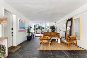 A modern living room with a sofa, two chairs, a coffee table, and a large mirror. There are potted plants and a poster on the wall. - Ocean-View Balcony + Shared Pool & Spa | Carbon Beach | Carbon & Coast (Malibu)