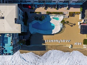 An aerial view of a hotel with a swimming pool, sun loungers, and a beach area.