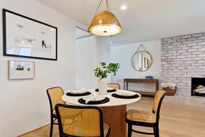 A dining area with a round table, four chairs, a hanging light fixture, and a brick wall.