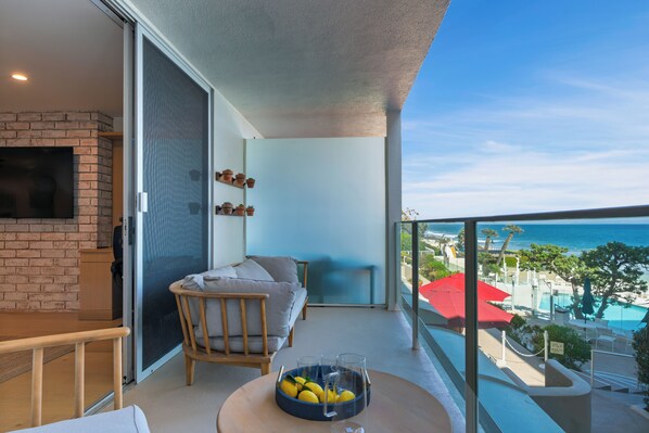 A balcony with a view of the sea, a seating area with a table, and a TV mounted on the wall.
