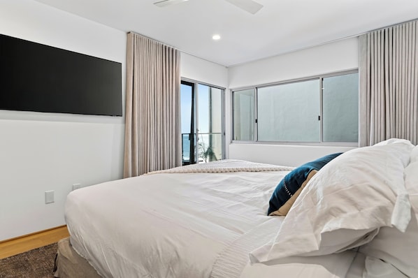 A modern hotel room with a large bed, a flat-screen TV, and a view of the ocean through the window.