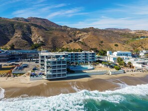 A coastal hotel with multiple buildings, a swimming pool, and a beach.