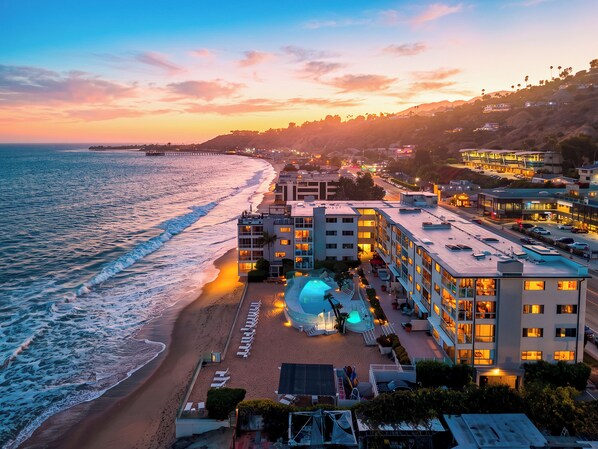 A beachfront hotel with a pool, multiple floors, and a view of the ocean.