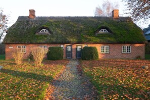 Ein Backsteinhaus mit Strohdach, einer Mittel-Tür und einem Kopfsteinpflasterweg, der dorthin führt.
