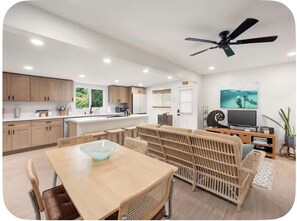 Una cocina moderna con armarios de madera, un comedor con un cuenco de vidrio como centro de atención y una sala de estar con sofá y televisión.