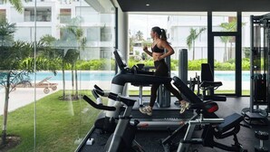 A modern gym with a treadmill, weight machines, and a view of a swimming pool and greenery. - 2BR Ground Floor Beach Retreat | Partial View (Las Terrenas)
