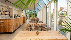A modern bar area with a wooden counter, wicker chairs, and a glass-enclosed dining space with a view of the outdoors. - Premium Waterfront Scandi Lodge (Wilsum)