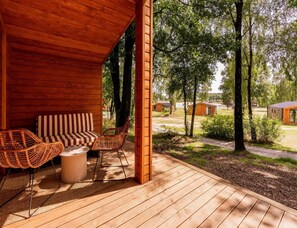 A wooden deck with outdoor furniture, a covered seating area, and a view of a forested area with cabins. - Premium Waterfront Scandi Lodge (Wilsum)