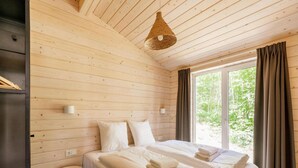A bedroom with a wooden ceiling, a bed with white linens, a bedside table, a wall-mounted light, and a window with curtains. - Premium Waterfront Scandi Lodge (Wilsum)