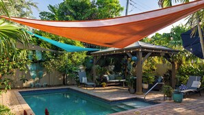 Um quintal com piscina, móveis de pátio e área de estar coberta.