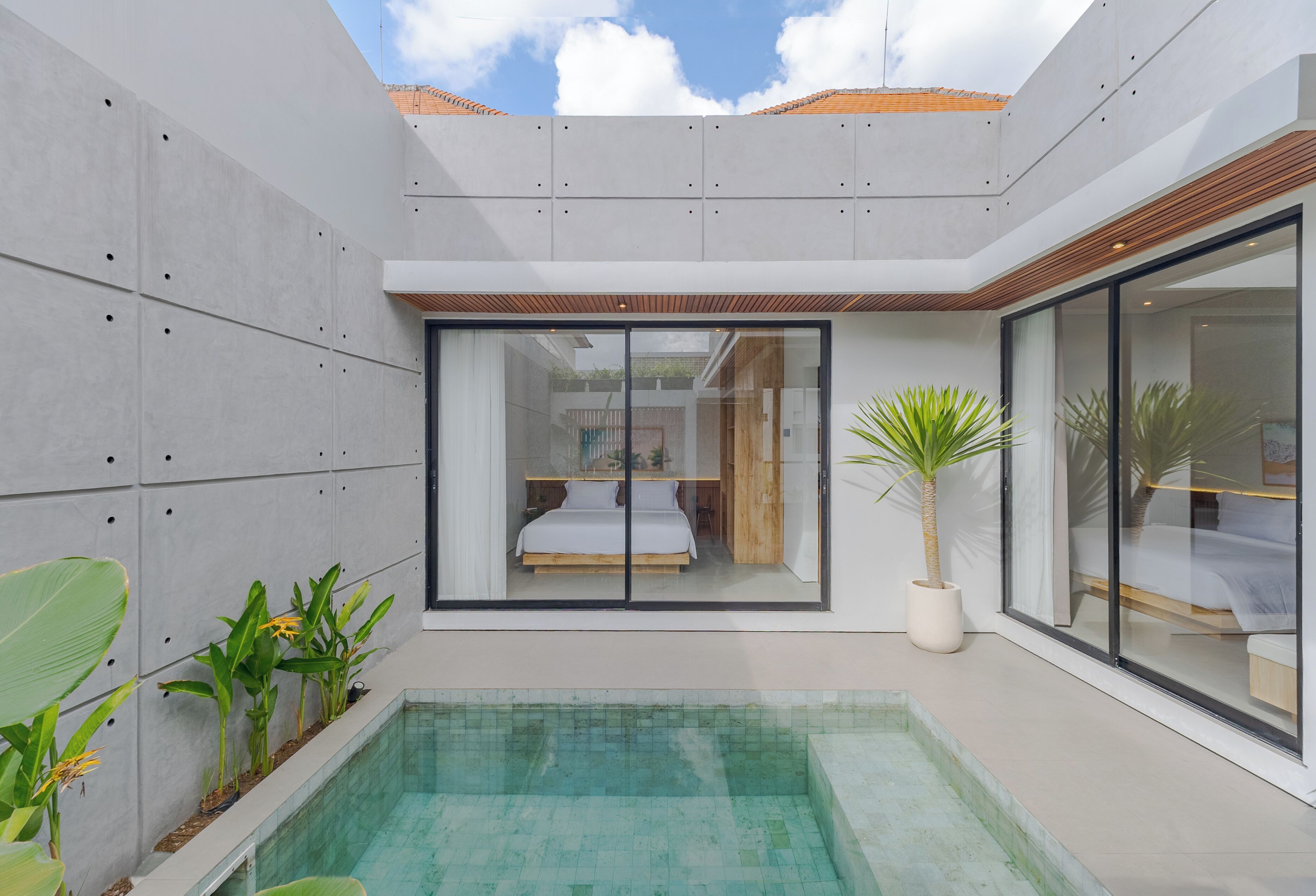 A modern interior with a glass-enclosed bedroom, a small pool, and potted plants.