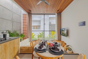 A dining area with a table set for two, a kitchen area with a stove, and a view of greenery outside. - Villa Kartal Altin by Pertama Stay (Badung Regency)