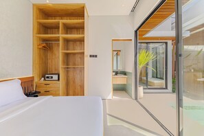 A modern hotel room with a large bed, a wooden wardrobe, a bathroom with a glass door, and a view of the outdoors. - Villa Kartal Altin by Pertama Stay (Badung Regency)