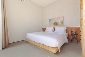 A hotel room with a bed, wooden headboard, a small table, and a chair. - Villa Kartal Altin by Pertama Stay (Badung Regency)