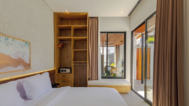 Ein modernes Hotelzimmer mit einem großen Bett, einem Holzschrank, einer kleinen Sitzecke und Blick durch eine Glastür.