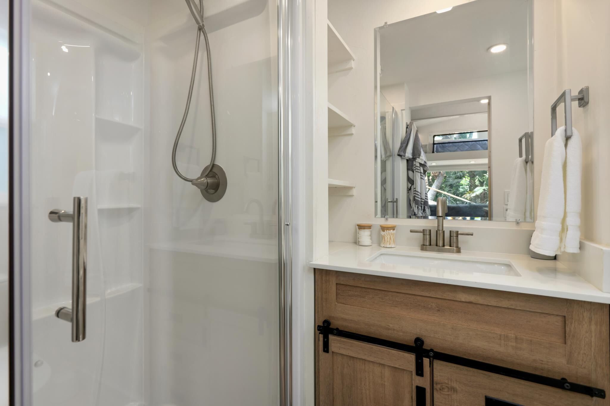 A modern bathroom with a glass shower enclosure, a wooden vanity with a sink, and a large mirror.